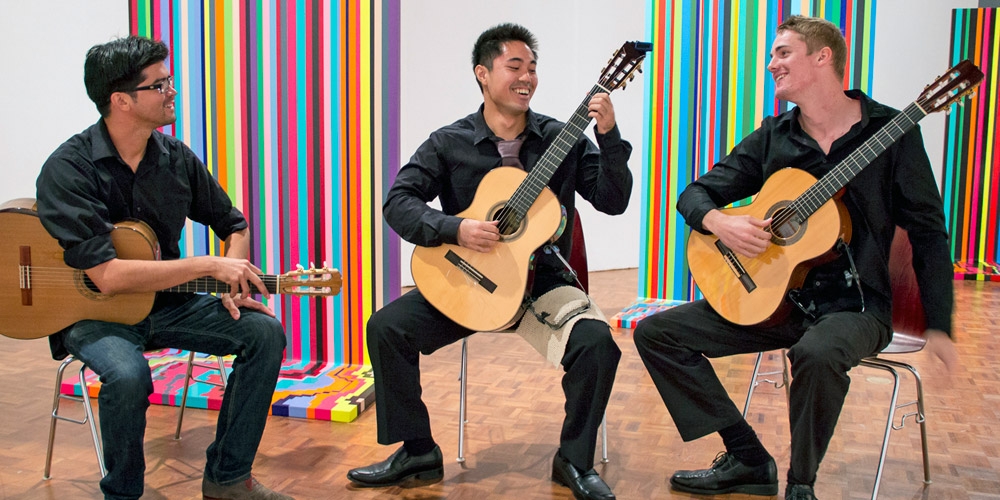 Ian O’Sullivan (left) with two of his students, playing music in front of MFA student Tom Walker's paintings at the Art Gallery. 