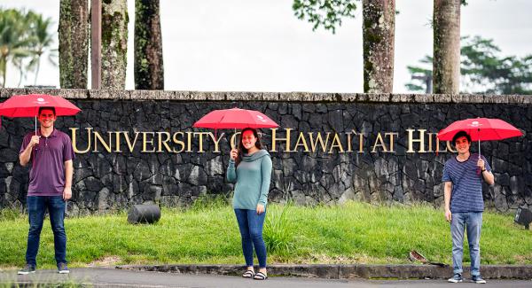 students with umbrellas in front of UH Hilo sign